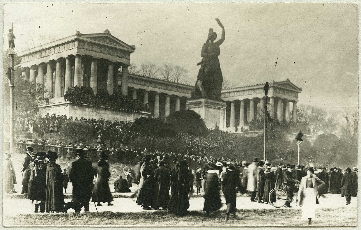 Friedenskundgebung auf der Theresienwiese in München am 7. November 1918 mit Blick auf die Statue der Bavaria und die Ruhmeshalle. Die Ruhmeshalle erinnert an berühmte Persönlichkeiten aus dem deutschen Sprachraum. Wie alle Bauten und Monumente der Ära König Ludwigs I. sollten auch Bavaria und Ruhmeshalle bayerische mit deutscher oder auch europäischer Identität verbinden.
